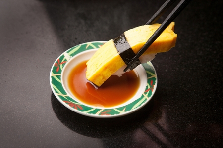 chopsticks holding egg sushi, dipping in soy sauceの写真素材