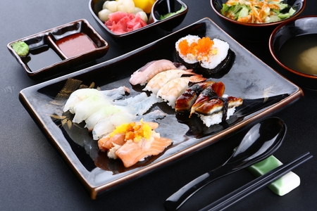sushi set on black plate served with soy sauce, spicy sauce, salads and picklesの写真素材