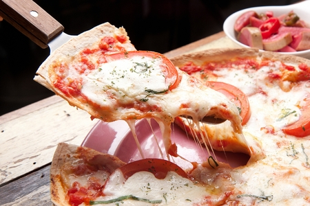 pizza knife lifting a slice of thin cheese tomato pizzaの写真素材