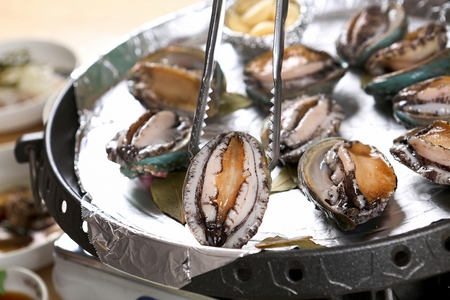 steamed abalones on pan, tong holding a abaloneの写真素材