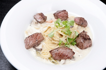 Steak cream pasta on a white plate, on a wooden tableの写真素材