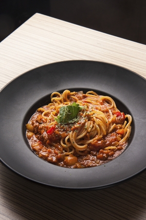 Bolognese pasta on a black plate, on a wooden tableの写真素材