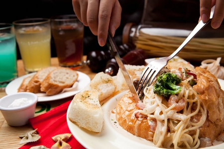 Hand cutting a mushroom cream paner pasta on a white plateの写真素材