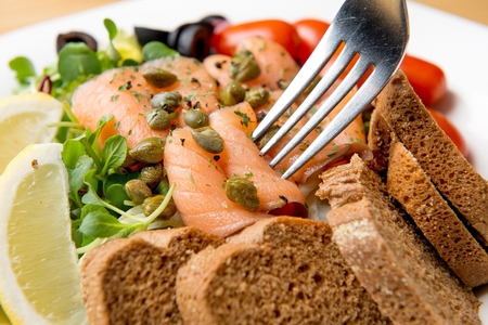 Salmon salad with thinly-sliced rye bread on a white plate, picked up by a fork, close-up