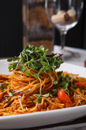 Arrabiata pasta on a white plate, beside a wine glass, on a talbeの写真素材