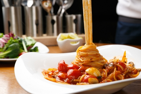 Chopsticks lifting up a pomodoro tomato pasta on a white plate, in a black background, close-upの写真素材