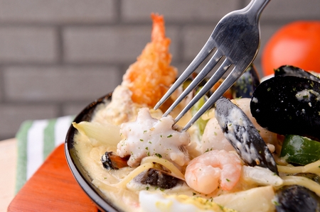 Fork lifting up a pescatore cream pasta on a black plate, close-upの写真素材