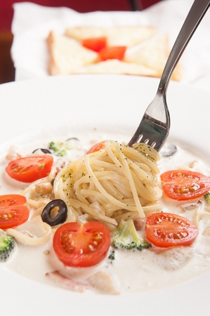 Fork lifting a cherry tomato carbonara pasta, on a white plate, close-upの写真素材