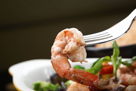 Fork lifting up a shrimp gambas from a wooden treyの写真素材