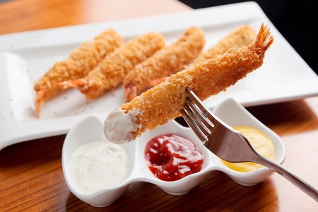 Fork dipping fried shrimp on a plate, on a tableの写真素材