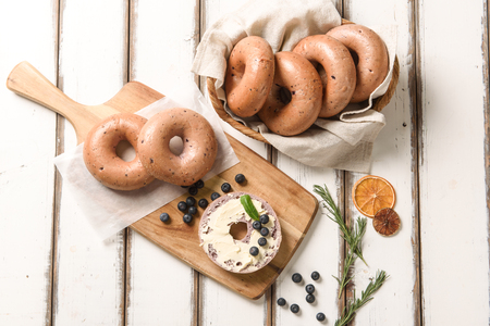 Blueberry bagel on wooden cutting board, and bagel in basketの写真素材