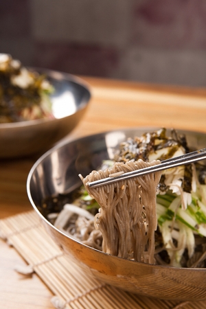 Chopsticks grabbing mulnaengmyeon, a korean cold noodle dish, in nickel silver bowlの写真素材