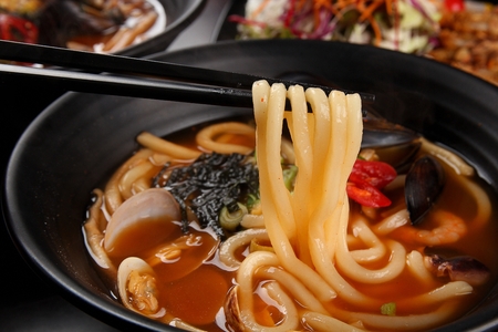 Chopsticks lifting udon from spicy broth, from black bowlの写真素材