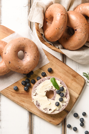 Blueberry bagel on wooden cutting board, and bagel in basketの写真素材