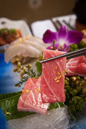Chopsticks grabbing tuna sashimi with gold dustの写真素材
