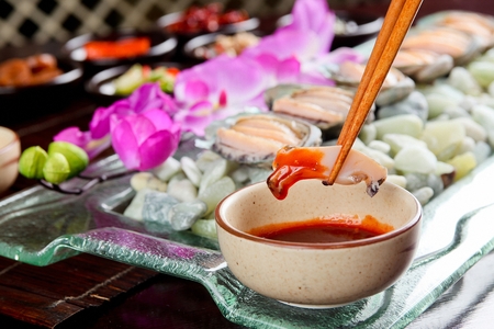 Chopsticks grabbing and dipping thinly sliced abalone in red chili pepper pasteの写真素材