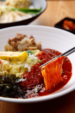 Chopsticks carrying Jjolmyeon, korean noodle cuisine, mixed in spicy sauce with various thinly sliced vegetables and boiled eggの写真素材