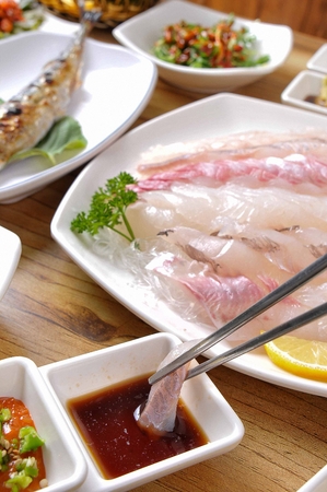 Chopstick grabbing sashimi and dipping it in red-chili pepper pasteの写真素材