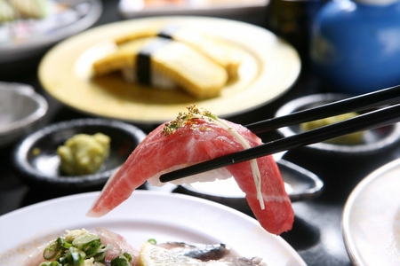 Chopsticks grabbing tuna sushi, a Japanese cuisine with gold dust, on a white plateの写真素材