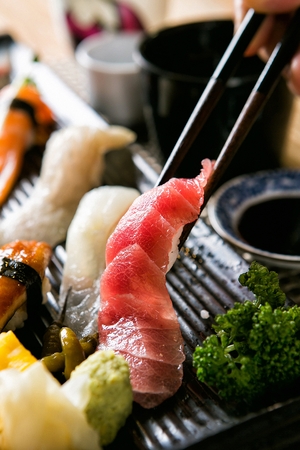 Chopstick picking up tuna sushi from a black plateの写真素材