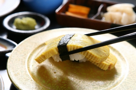Chopsticks grabbing egg sushi, a Japanese cuisine, on a yellow plateの写真素材