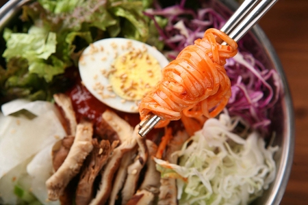 Chopsticks grabbing bibimguksu, a korean cuisine of noodles that are mixed with spicy sauce and vegetables, on silver plateの写真素材
