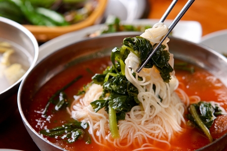 Chopsticks grabbing yeolmu guksu, a korean noodle cuisine with young radish kimchi and boiled eggs, on silver bowlの写真素材