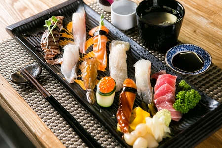 Beef sushi, salmon sushi, tuna sushi, flatfish sushi, soy sauce marinated shrimp sushi, chopsticks, soy sauce on a black plateの写真素材