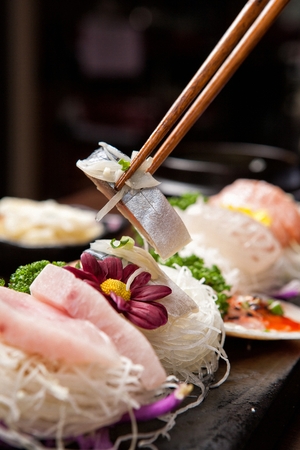 Chopsticks grabbing mackerol sashimi, on a black plateの写真素材