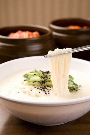Chopsticks grabbing Kongguksu, korean noodle cuisine, broth is made of grated beans; served with cucumber, on white bowlの写真素材