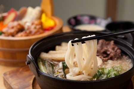 Chopsticks grabbing udon, japanese noodles with fried tofu and boiled eegs, on black potの写真素材