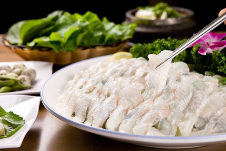 Chopsticks grabbing Rockfish sashimi, raw rockfish sliced thinly, on a white round plateの写真素材