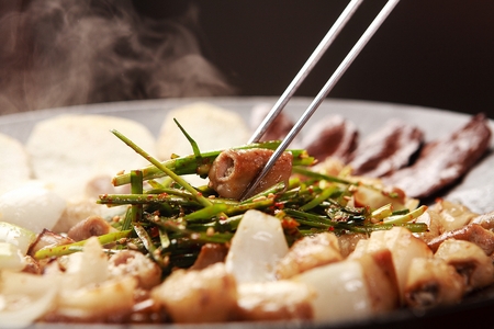 Chopsticks grabbing beef makchang with chives, being grilledの写真素材