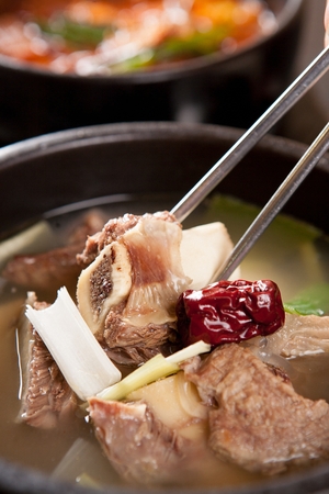 Chopsticks grabbing rib inside short rib soup, a Korean cuisine, boiled with short ribs, in a black potsの写真素材