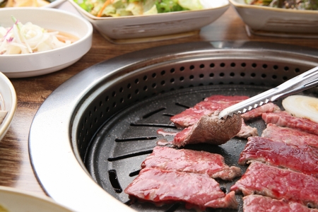 Tongs turning bottom sirloin, being grilled, on a black grillの写真素材