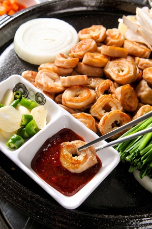 Chopsticks grabbing grilled pork makchang and dipping in red pepper paste after grilled on a black grillの写真素材