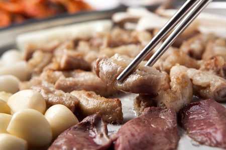 Chopsticks grabbing beef makchang, being grilledの写真素材