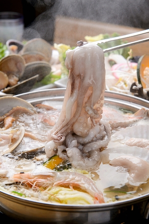 Tongs grabbing small octopus boiling in seafood stewの写真素材