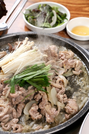 Raw duck with enoki mushroom and chives, being cooked, on a black grillの写真素材
