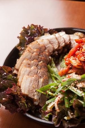 Bossam, a Korean cuisine, boiled pork, with marinated chives, on a black round plateの写真素材