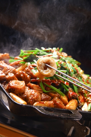 Chopsticks grabbing marinated pork makchang being grilled on a black grillの写真素材