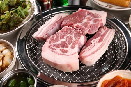 Pork neck slices being grilled, on a grill placed over charcoalの写真素材