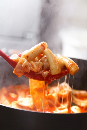 Ladle lifting tteokboki, a Korean cuisine, rice cake and fish cakes stir-fried with spicy sauce, in a black potの写真素材