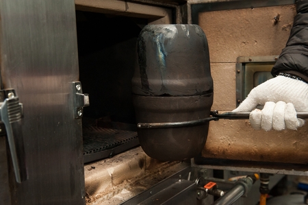 Chef's hand placing a black pot with duck inside a hot oven