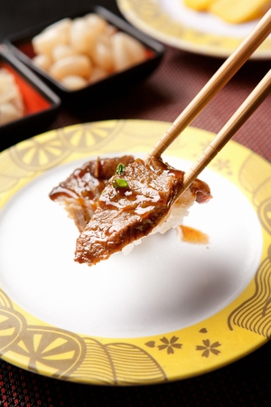 Chopsticks grabbing beef sushi, on a round plateの写真素材
