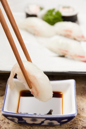 Chopsticks grabbing flatfish sushi and dipping in soy sauceの写真素材