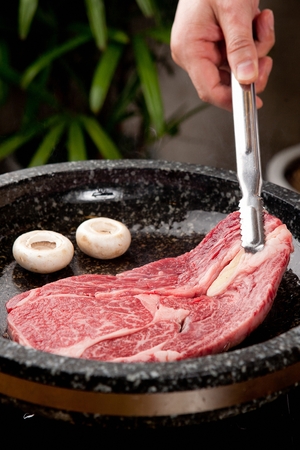 Tongs grabbing beef sirloin, being grilled, on a black grillの写真素材