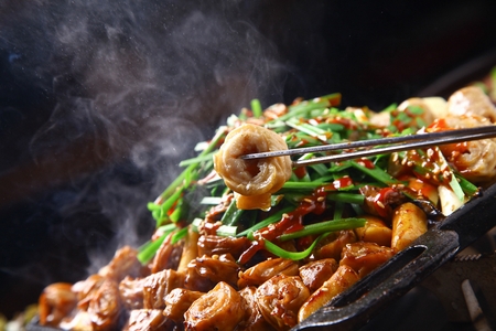 Chopsticks grabbing pork makchang, being grilled, on a black grillの写真素材