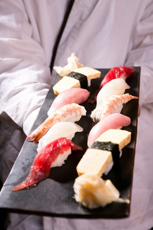 Japanese chef grabbing black plate with assorted sushiの写真素材