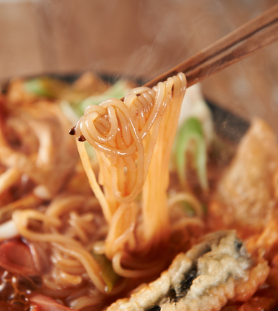 Chopsticks grabbing noodles of tteokbokki, stir-fried with fish cakes and vegetables in brothの写真素材